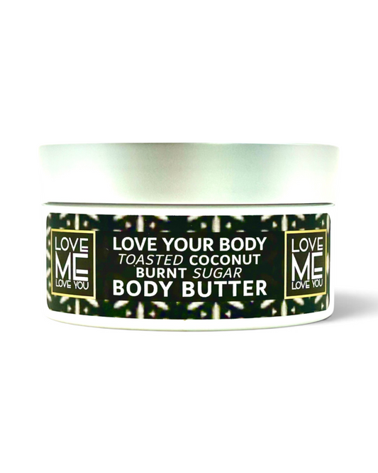 A jar of Love Me Body Butter in the Toasted Coconut Burnt Sugar scent, featuring a white container with a black and green patterned label and a silver lid, set against a plain white background.